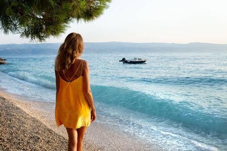 Young beautiful girl looking at boat and sea waves at resortの写真素材