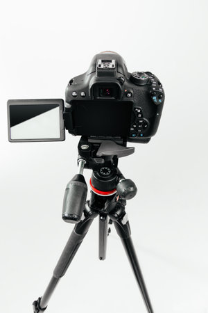 Photo camera with a tilting LCD screen on the tripod back view. Studio shot on white background
