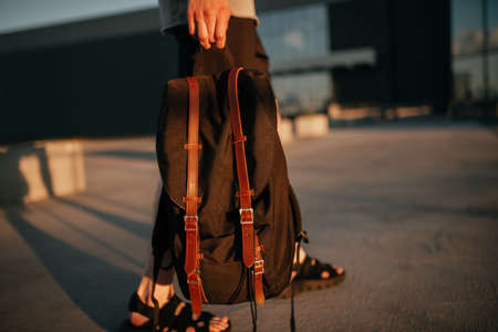 Unrecognizable model wearing casual outfit and holding black famous backpack. Gray clothing in trendy minimalistic style. Street fashion for spring or fall season. Details of everyday look.の写真素材