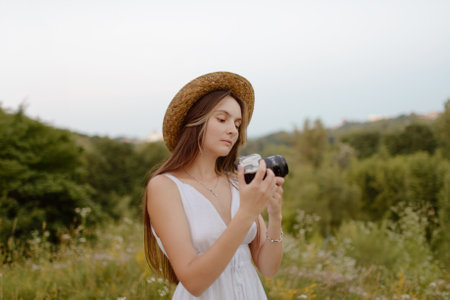 A young woman in a stylish hat joyfully captures beautiful moments while enjoying photography in natureの写真素材