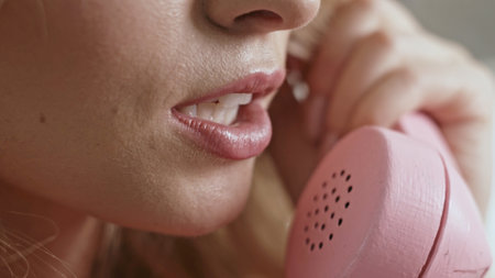 A closeup view of a Woman Engaged in Conversation While Using a Vintage Pink Telephone