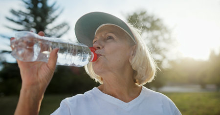 An Elderly Woman Happily Drinking Refreshing Water While Enjoying the Outdoors in Sunlight