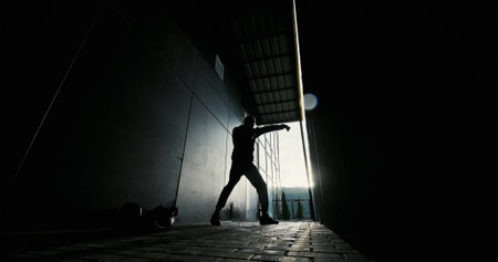 The striking silhouette of a man caught in action within a dark and shadowy alleywayの写真素材