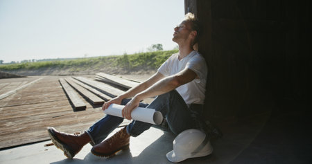 A contemplative worker at a busy construction site reviews plans, deep in thoughtの写真素材