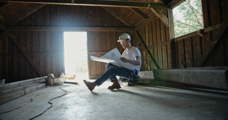 A man is deeply analyzing the intricate blueprints in a rustic barn environmentの写真素材