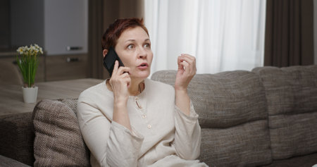 Frustrated Woman Engaged in a Phone Call While Sitting Comfortably in a Cozy Living Room Spaceの写真素材