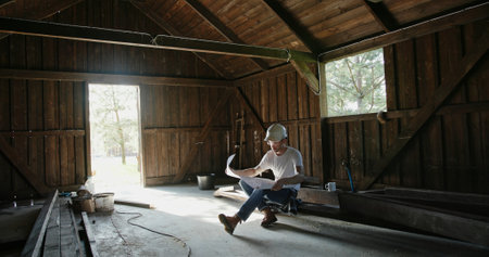 A Man is Engaged in Work Inside a Rustic Barn Surrounded by Tools and Detailed Plansの写真素材