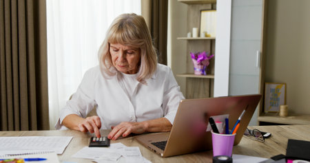 A Focused Woman Diligently Working from Home Surrounded by a Calculator and Laptop