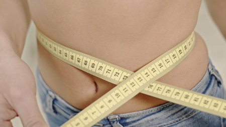 Crop woman measuring waistline. Faceless shot of shaped woman measuring waist with tape.