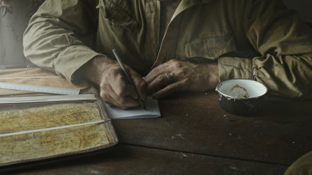 Soviet Army soldier analyzes map and draws up action plan sitting in abandoned house at table near...