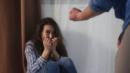 An angry man threatens to beat his wife, and she covers her face with her hands in fear.