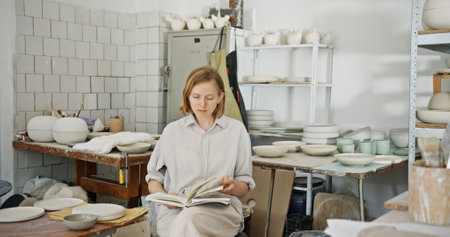 Female Potter Reviewing Notes in Busy Pottery Studio