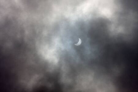 Real astronomical picture of a solar eclipse, as seen in a cloudy dayの写真素材