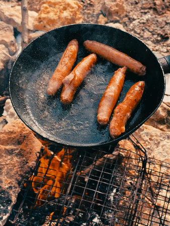 Sausages are fried in a frying pan. Picnic. Tourist lunch. Picnic. Fastfood. Grilled sausages on grill with smoke and flameの写真素材