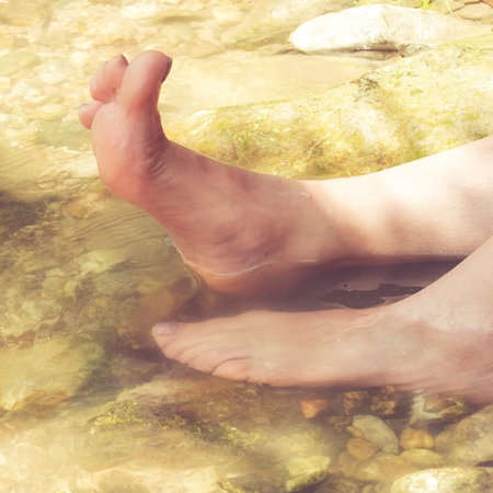 Girl cools her feet down in crystal clear mountain water on a hot summer day. Pleasure and Enjoyの写真素材