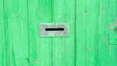 A Hole in the fence designed to receive letters. The wooden fence is painted in a vibrant green colorの写真素材