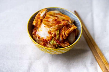 Kimchi in small plate with chopsticks on light fabricの写真素材