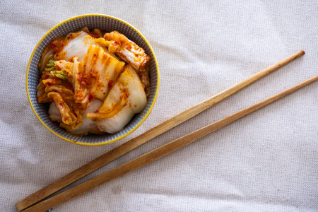 Kimchi in small plate with chopsticks on light fabricの写真素材