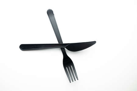 Clean plastic black forks and knives on white background. Disposable dishes, environmental...