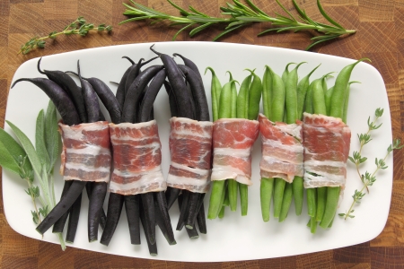 Colored beans wrapped in bacon slices on a plateの写真素材