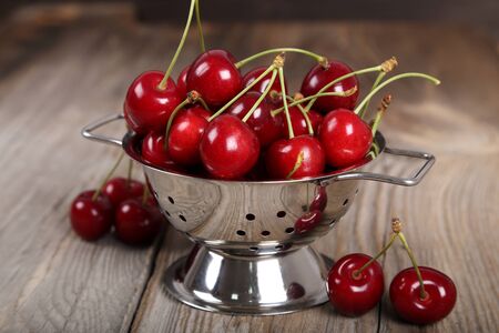 Ripe, fresh cherries in a small colander on a wooden backgroundの写真素材