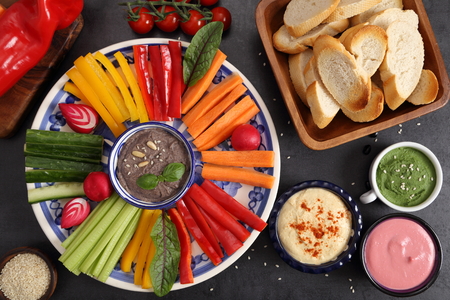 Colorful fresh vegetables cut into strips on a plate and various types of humus.