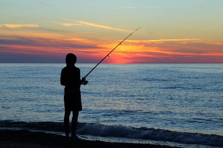 Silhouette of an angler by the sea against the  setting sun.の写真素材