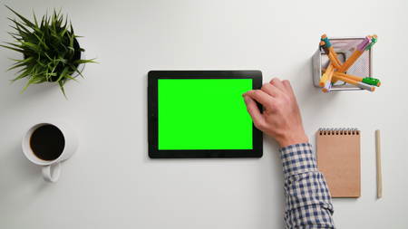A mans finger scrolling on the green touchscreen. A tablet is on the white table. View from the top. Close-up.の写真素材