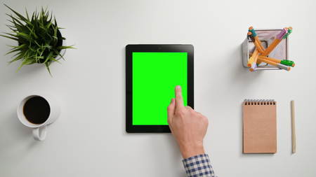 A mans finger touching an tablet  with a green screen. A tablet is on the white table. View from the top. Close-up.の写真素材
