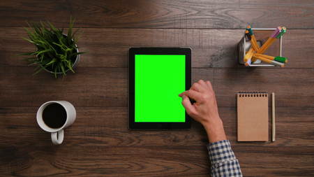 A mans finger scrolling on the green touchscreen. The i-Pad is on the brown table. View from the top. Close-up.の写真素材