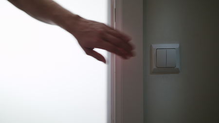 A hand switching on the light in a dark room. Close-up shotの写真素材