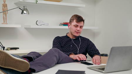 A young man sitting and listening to music indoors. Medium Dolly shot.の写真素材