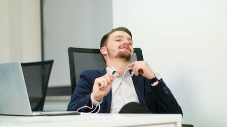A young businessman singing and listening to music in the office. Medium shot.の写真素材