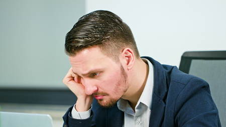 A tired young businessman working overtime in the office. Close-up shot. Soft focus.の写真素材