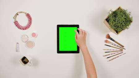 A lady's finger scrolling on the green touchscreen of a tablet. The tablet is on the white table. View from the top. Close-up.の写真素材