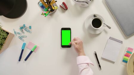 Lublin, Poland - November 2017: A finger scrolling on a phone with a green screen. The phone is on the white table. View from the top. Close-up.のeditorial素材