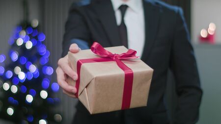 Closeup of a mans hand holding and offering a Christmas gift or present. A happy husband concept. Soft focusの写真素材