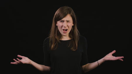 A beautiful young lady showing a What gesture against a black background. Medium Shotの写真素材