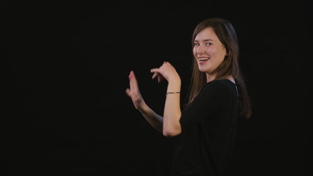 A beautiful young lady showing I am happy gesture against a black background. Medium Shotの写真素材
