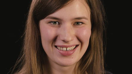 A beautiful young ladys face smiling against a black background. Close-up shot