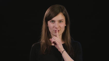 A beautiful young lady showing a shhh meme against a black background. Medium Shotの写真素材