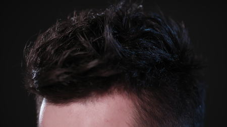 A young man touching his hair against a black background. Close-up macro shot