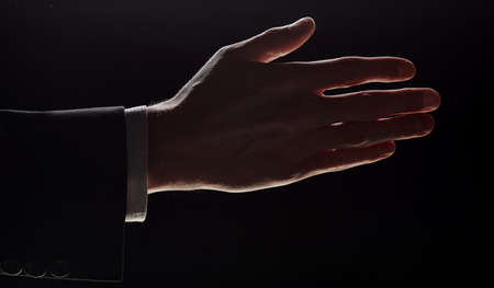 A man holds out his hand for a handshake, highlighted on a black backgroundの写真素材
