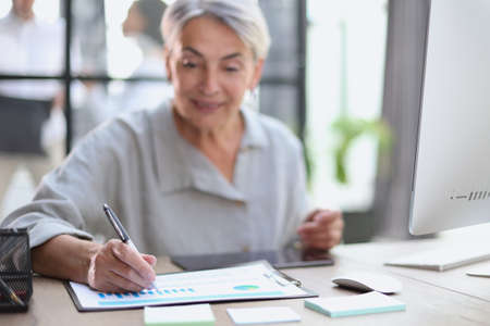 The older stylish woman takes notes in a documentの写真素材
