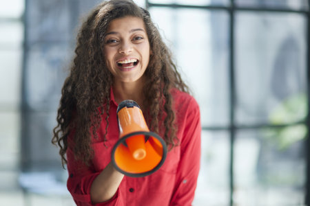 Beautiful girl shouting into a megaphone in a modern officeの写真素材
