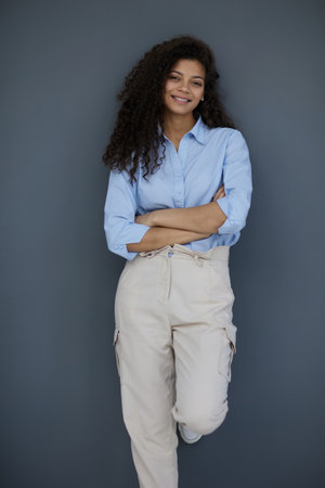Smiling attractive young business woman in blue shirt posing on gray background