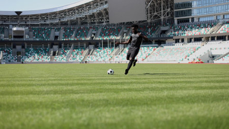 African American man playing football on the stadium field. A man runs with a soccer ball across the field.の写真素材