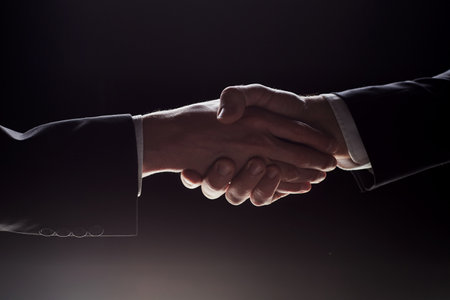 Photo of two men in suits shaking hands on a black background