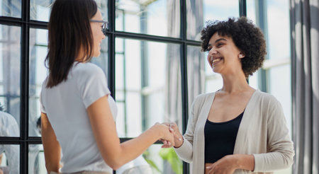 Two Businesswomen Shaking Hands In Modern Office