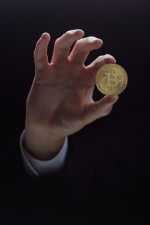 A hand holds a coin isolated on a black backgroundの写真素材